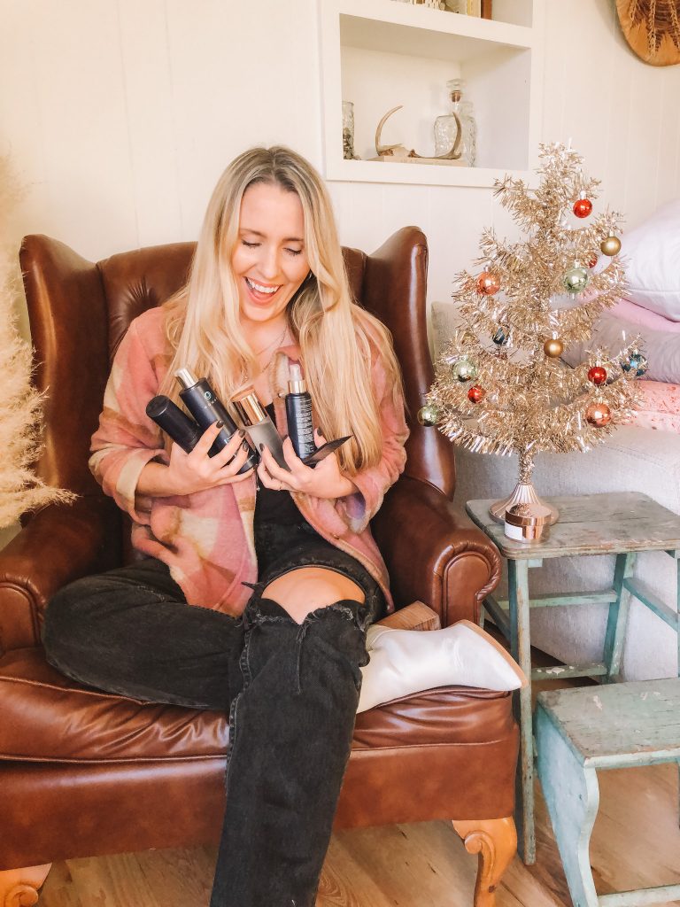 Monat Sale by popular beauty blog, Pearls and Twirls: image of a woman sitting in a leather chair next to a gold tinsel Christmas tree and holding Monat products in her hands. 