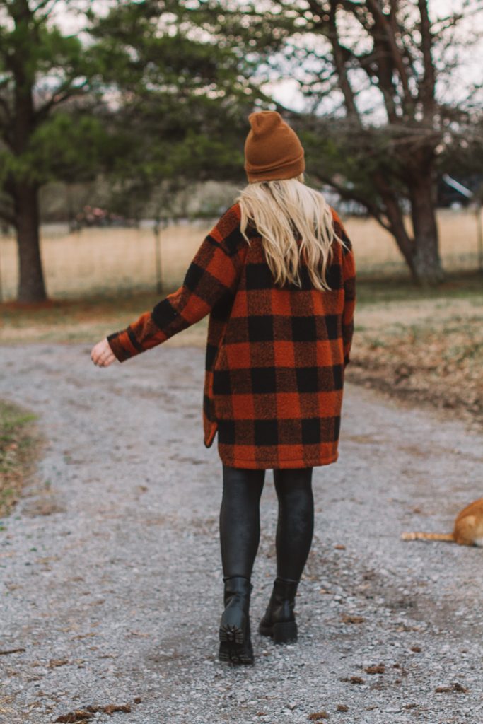 shacket and leggings |shacket and leggings outfit | Old Navy Shacket by popular Nashville fashion blog, Pearls and Twirls: image of a woman standing outside on a gravel road and wearing a Carhart beaning, Old Navy orange and black buffalo plaid shacket, black Spanx faux leather leggings, Target combat boots, and My Kind of Lovely swing top.